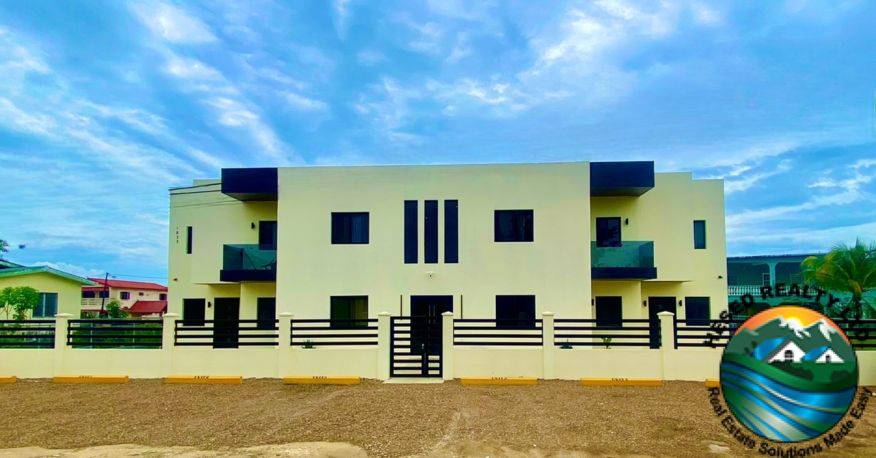 Front exterior view of a modern two-storey apartment building on Lily Street, Belmopan, with private balconies and tinted glass railings.