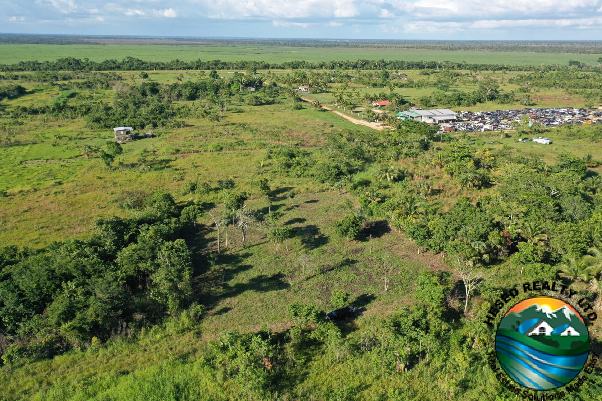 Aerial view of a 1-acre property in Harmonyville Village, Belize, adjacent to the George Price Highway, showing accessible land near Belmopan with utility connections.