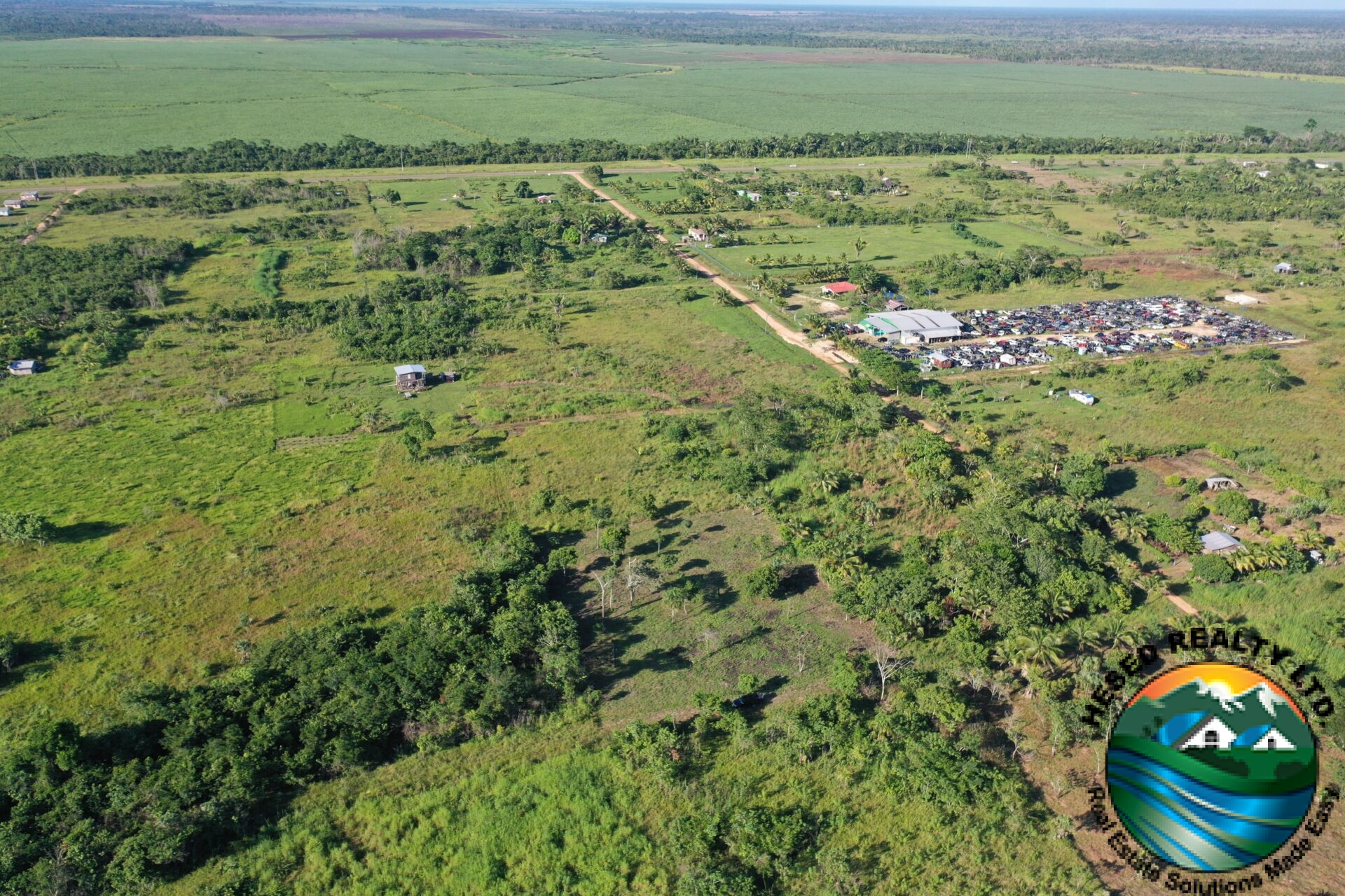 Aerial view of a 1-acre property in Harmonyville Village, Belize, adjacent to the George Price Highway, showing accessible land near Belmopan with utility connections.