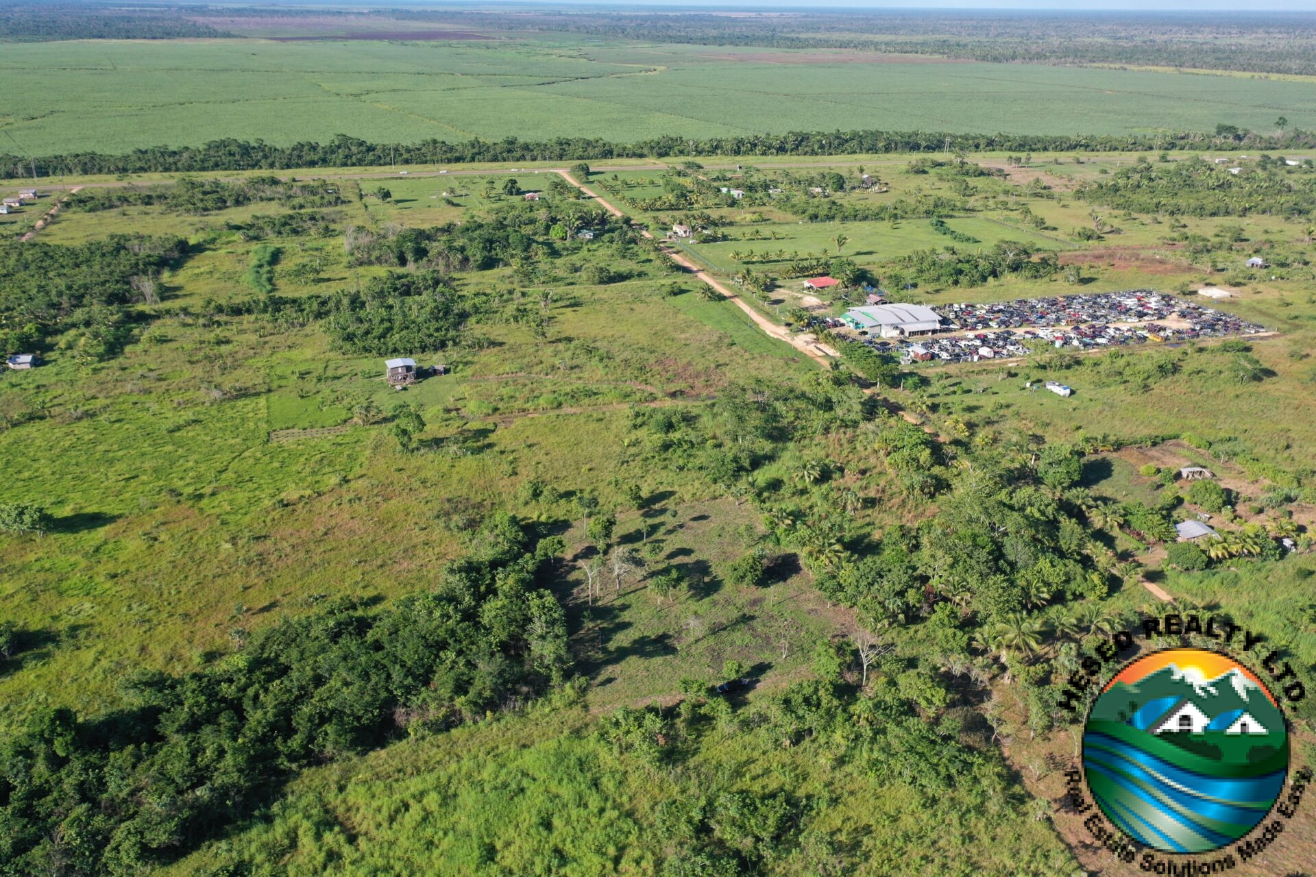 Aerial view of a 1-acre property in Harmonyville Village, Belize, adjacent to the George Price Highway, showing accessible land near Belmopan with utility connections.