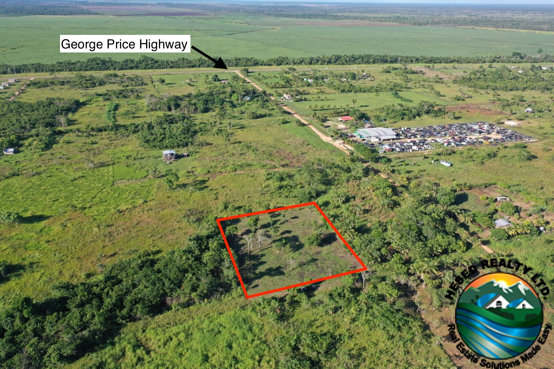 Aerial view of a 1-acre property in Harmonyville Village, Belize, adjacent to the George Price Highway, showing accessible land near Belmopan with utility connections.